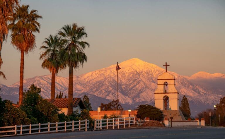 Stunning view of The Asistencia chapel with snow-capped mountains at sunset in Redlands, CA.